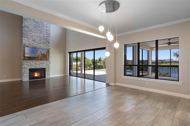 unfurnished living room featuring crown molding, baseboards, a stone fireplace, wood finished floors, and a ceiling fan