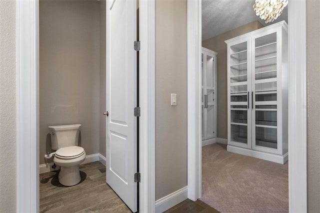 bathroom featuring an inviting chandelier, toilet, baseboards, and wood finished floors