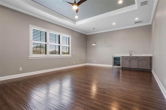 unfurnished living room with beverage cooler, visible vents, wet bar, a tray ceiling, and dark wood-style flooring