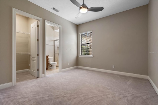 unfurnished bedroom featuring visible vents, light colored carpet, a walk in closet, and baseboards