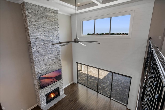 living room featuring ornamental molding, a fireplace, a towering ceiling, wood finished floors, and a ceiling fan