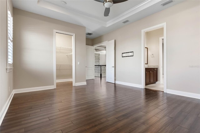 unfurnished bedroom with a tray ceiling, a spacious closet, wood finished floors, and visible vents