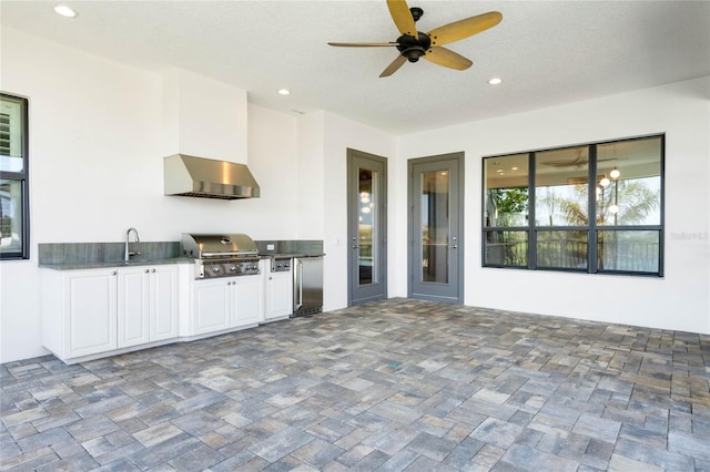 interior space with ceiling fan, wall chimney range hood, high end refrigerator, recessed lighting, and white cabinetry