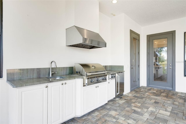 kitchen with refrigerator, a sink, white cabinets, a textured ceiling, and wall chimney exhaust hood