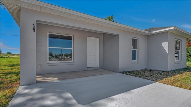 entrance to property featuring stucco siding, a lawn, and a patio area