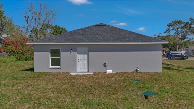 back of property featuring a yard, roof with shingles, and stucco siding