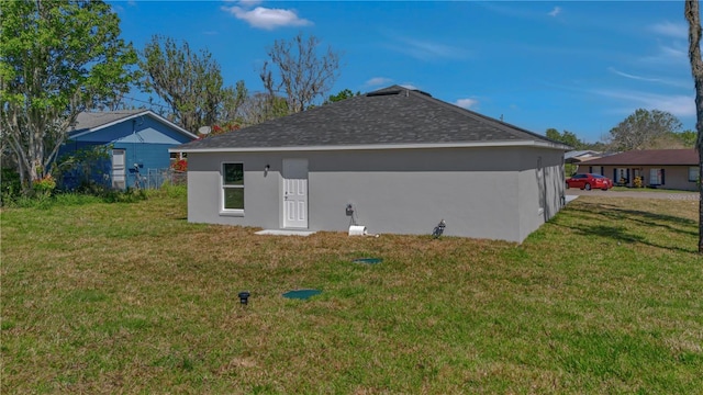 back of property featuring stucco siding, a shingled roof, and a yard