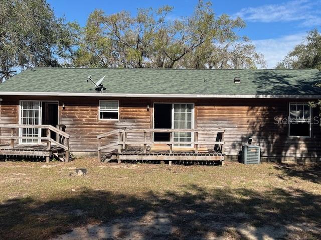 back of property with a lawn, central AC, a deck, and roof with shingles