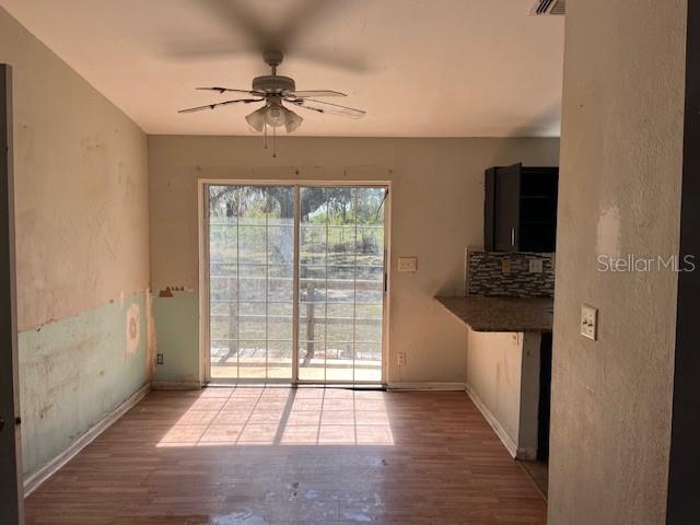 unfurnished dining area with a ceiling fan, visible vents, wood finished floors, and baseboards