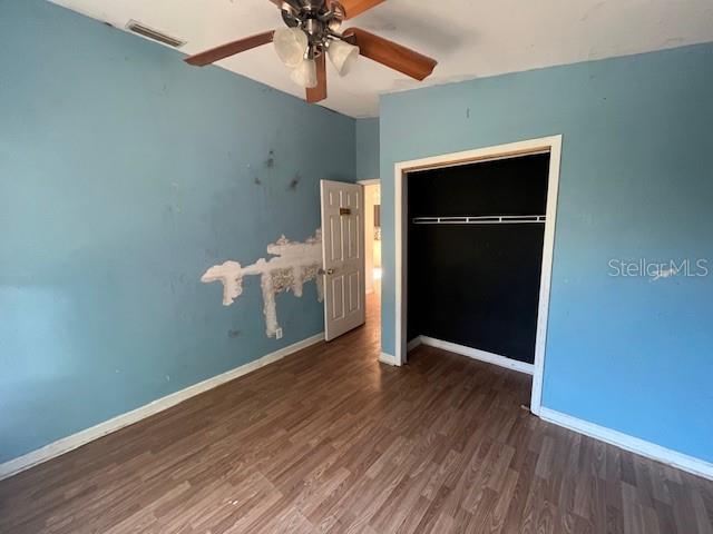 unfurnished bedroom with wood finished floors, visible vents, a closet, and baseboards