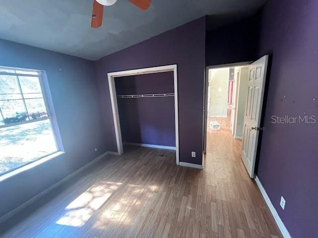 unfurnished bedroom with lofted ceiling, wood finished floors, a closet, and baseboards