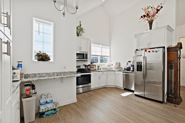 747 Fraser Ct, Kissimmee, FL 34759 - kitchen featuring white cabinets, stainless steel appliances, light wood-style flooring, light stone countertops, and high vaulted ceiling