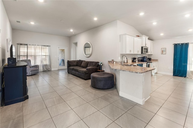 kitchen featuring stainless steel appliances, light stone countertops, open floor plan, and white cabinetry