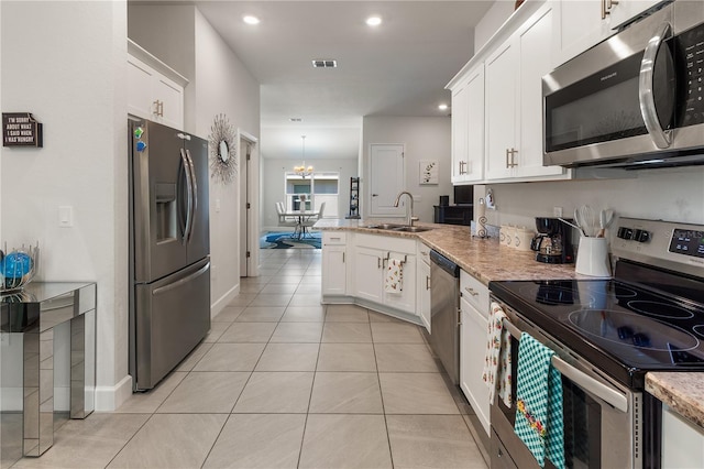 kitchen with a peninsula, stainless steel appliances, light tile patterned flooring, white cabinetry, and a sink