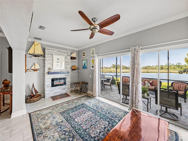 living room with visible vents, a water view, ornamental molding, a ceiling fan, and a glass covered fireplace