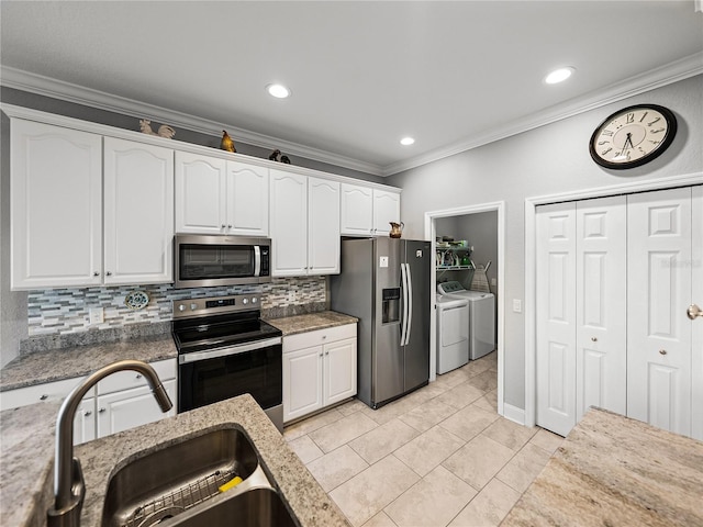 kitchen with washer and dryer, a sink, white cabinetry, stainless steel appliances, and crown molding