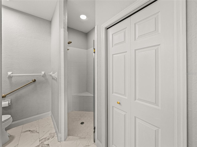 bathroom featuring marble finish floor, toilet, a shower stall, and baseboards