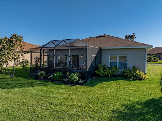 back of property featuring glass enclosure, a yard, roof with shingles, and stucco siding