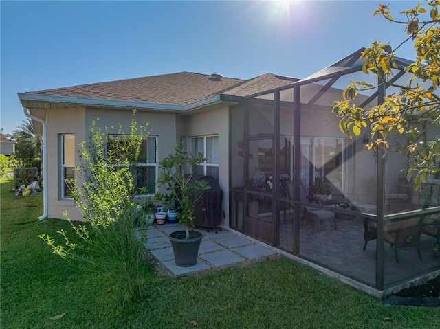 back of house with a patio, a yard, a shingled roof, stucco siding, and a lanai