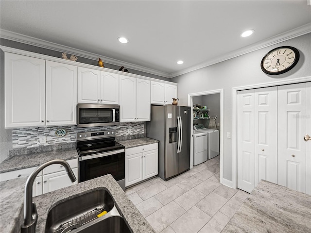 kitchen featuring a sink, appliances with stainless steel finishes, white cabinets, crown molding, and washing machine and clothes dryer