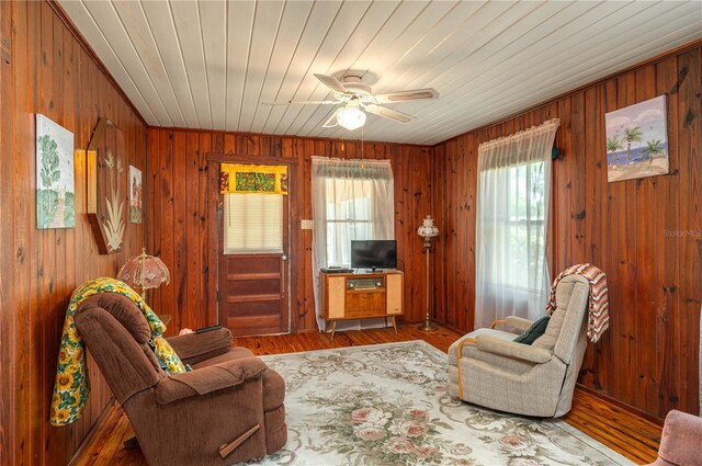 living area featuring wooden ceiling, wooden walls, wood finished floors, and ceiling fan