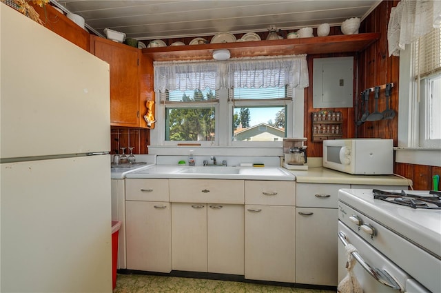 kitchen featuring white appliances, electric panel, a sink, light countertops, and wood walls