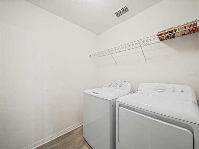 laundry area with visible vents, wood finished floors, separate washer and dryer, baseboards, and laundry area