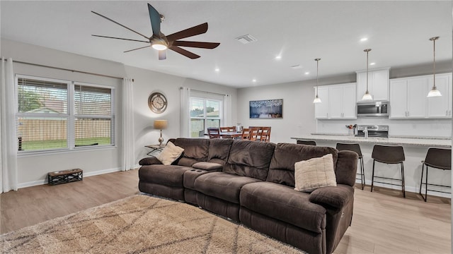 living room featuring light wood-type flooring, visible vents, a ceiling fan, recessed lighting, and baseboards