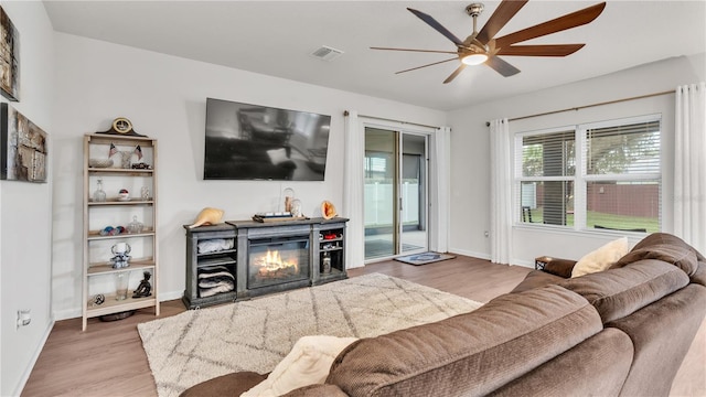 living area featuring wood finished floors, baseboards, visible vents, ceiling fan, and a glass covered fireplace