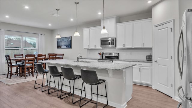 kitchen with an island with sink, a sink, a kitchen breakfast bar, appliances with stainless steel finishes, and light wood finished floors