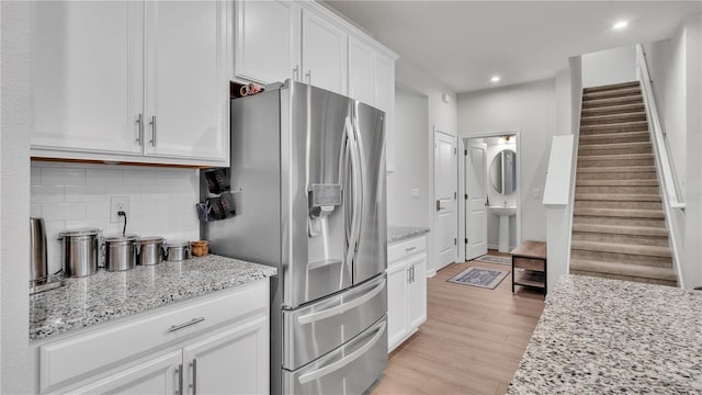 kitchen featuring light stone countertops, light wood-type flooring, decorative backsplash, white cabinetry, and stainless steel fridge