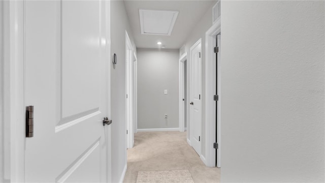 corridor featuring visible vents, light carpet, baseboards, and attic access