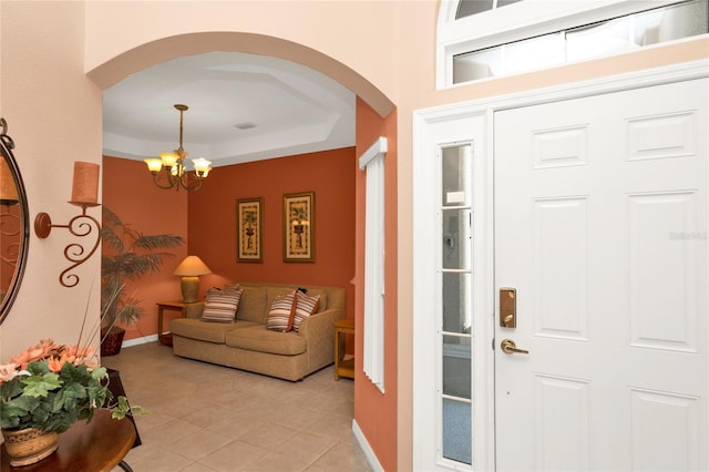 foyer entrance featuring baseboards, a tray ceiling, an inviting chandelier, light tile patterned flooring, and arched walkways