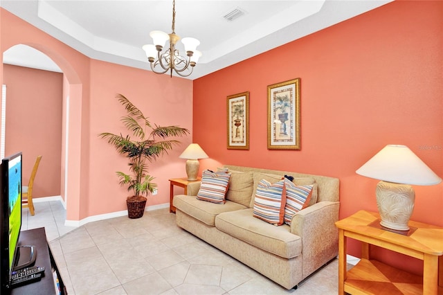 living area with visible vents, baseboards, a tray ceiling, an inviting chandelier, and arched walkways