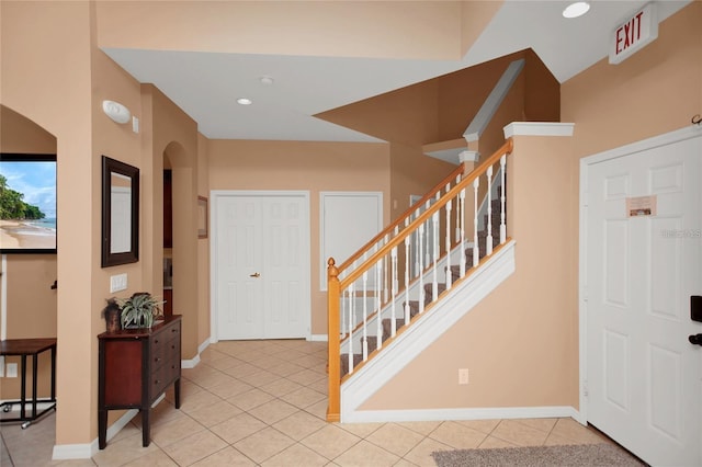 foyer entrance with stairs, light tile patterned floors, and arched walkways