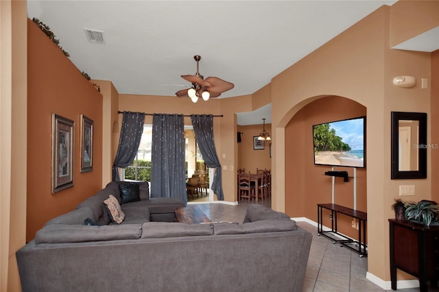 living area with light tile patterned floors, a ceiling fan, visible vents, baseboards, and arched walkways