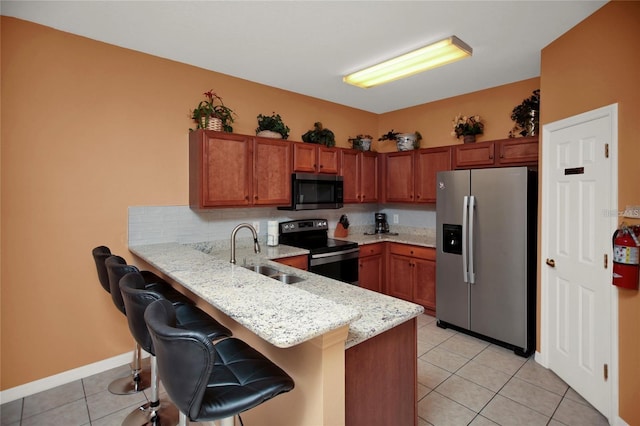 kitchen with light tile patterned floors, a peninsula, a kitchen breakfast bar, stainless steel appliances, and a sink