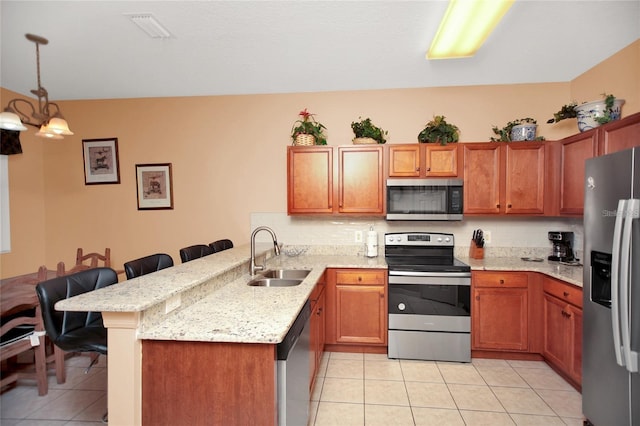 kitchen with a sink, a kitchen breakfast bar, appliances with stainless steel finishes, a peninsula, and light tile patterned floors