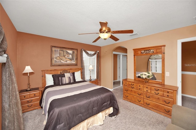 carpeted bedroom with baseboards, visible vents, arched walkways, ceiling fan, and a textured ceiling