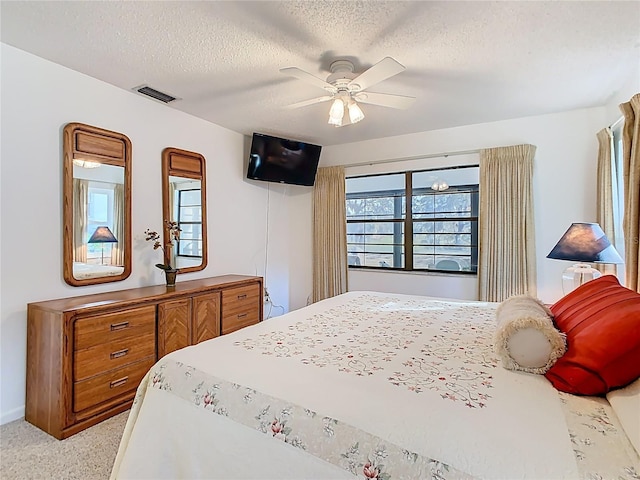 bedroom with ceiling fan, light colored carpet, visible vents, and a textured ceiling