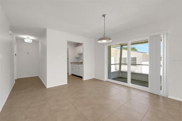 empty room featuring a sink, light tile patterned floors, baseboards, and a textured ceiling