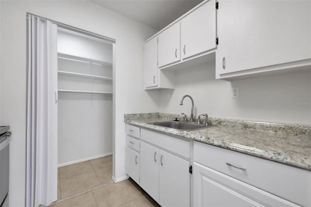 kitchen with baseboards, light tile patterned flooring, a sink, light countertops, and white cabinetry