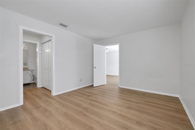 unfurnished bedroom featuring visible vents, connected bathroom, baseboards, light wood-style flooring, and a closet