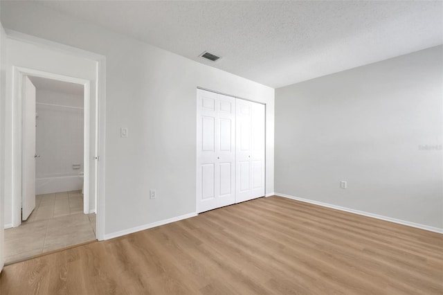 unfurnished bedroom with visible vents, a textured ceiling, a closet, light wood-style floors, and baseboards