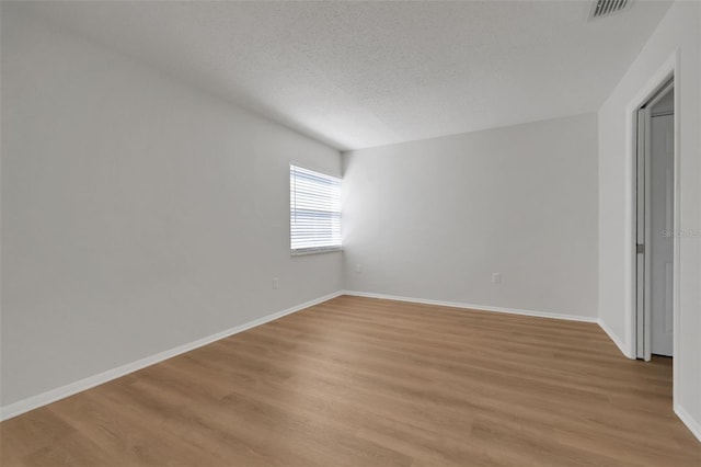 unfurnished room featuring light wood-style flooring, baseboards, visible vents, and a textured ceiling