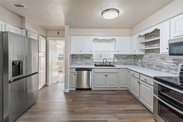 kitchen with a sink, white cabinetry, stainless steel appliances, light countertops, and dark wood-style flooring