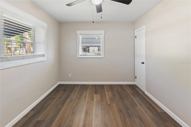 empty room with dark wood finished floors, a ceiling fan, and baseboards