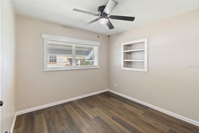 empty room featuring dark wood finished floors, built in features, a ceiling fan, and baseboards