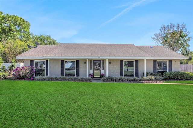 ranch-style home with brick siding, roof with shingles, a front lawn, and fence