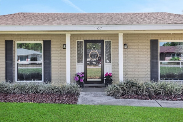 entrance to property with brick siding and a shingled roof